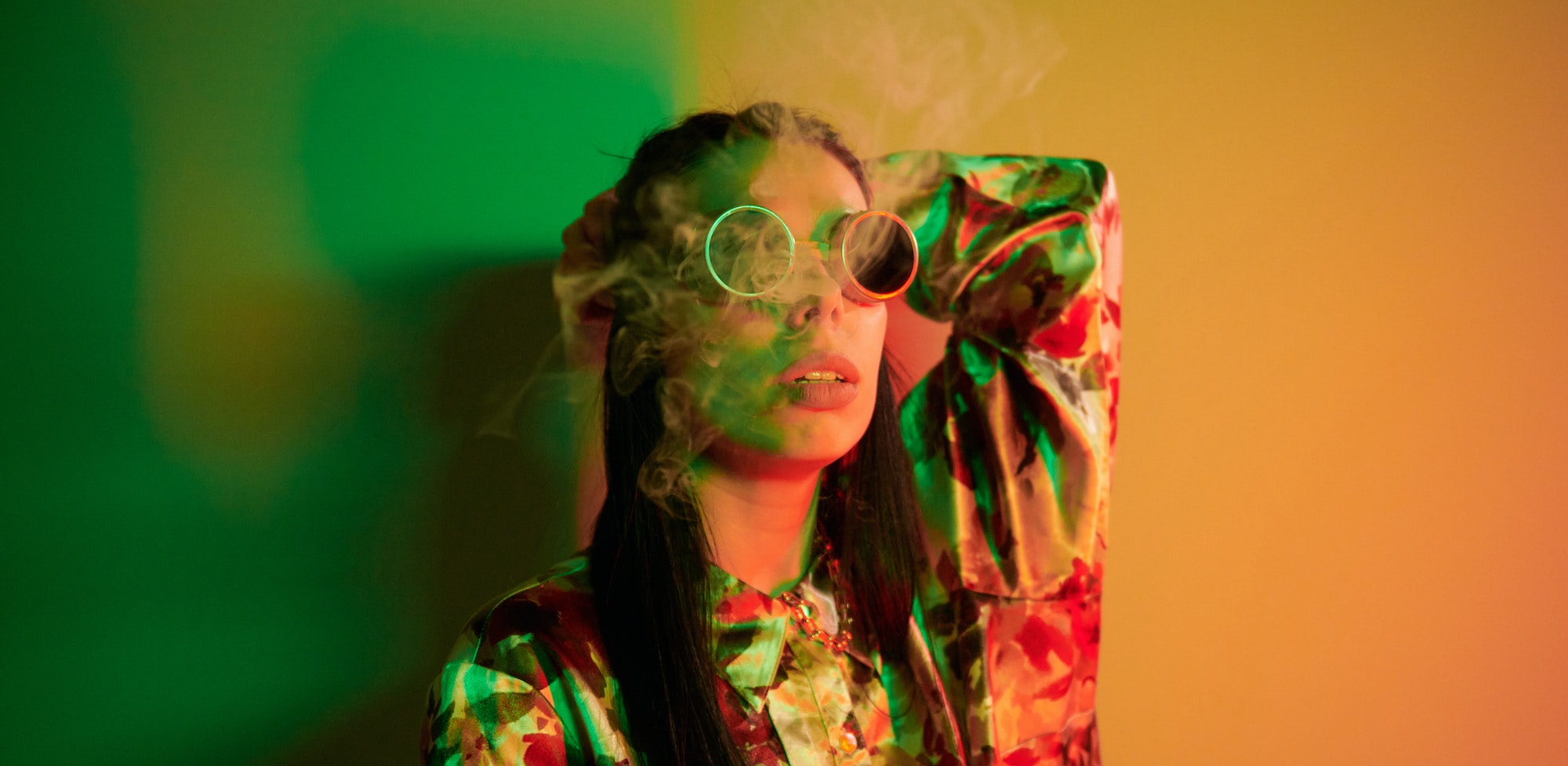 Smoking, activity. Fashionable young woman standing in the studio with neon light